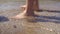 Child feet barefoot walk along a shore. Â Picks up a black float thrown by surf